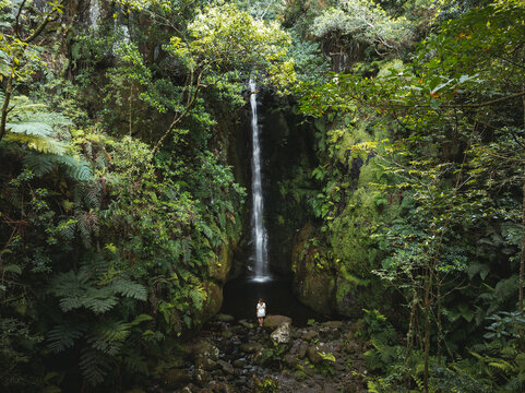 Aerial view of Rabo do Burro waterfall cascading into a pool surrounded by lush ferns and mossy rocks with a person in white standing at the base Ponta Delgada, Madeira, Portugal.
