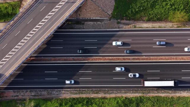 Top-down view of a busy motorway with cars and a red truck passing under an overpass bridge, surrounded by green verges