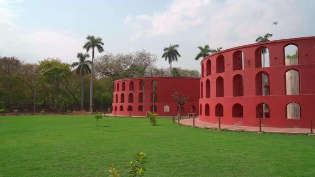 A wide static shot of the Rama Yantra, two large cylindrical structures used to measure the altitude and azimuth of celestial bodies, located in the lush gardens of Jantar Mantar, New Delhi.