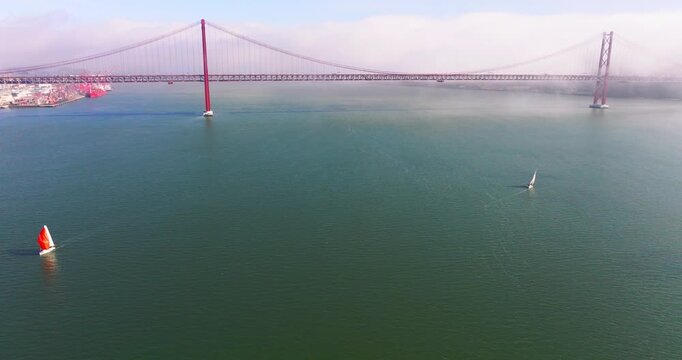 Aerial establishing shot of the 25th April Bridge emerging from coastal fog over the Tagus