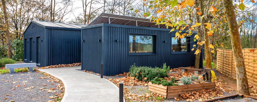 Contemporary modular office constructed from shipping containers with dark facade and rooftop solar panels, pathway and raised garden beds with autumn leaves showcasing eco friendly building in nature