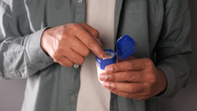 Man dipping index finger into blue jar of white petroleum jelly for skin care maintenance.