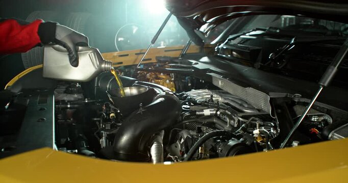 Super slow motion wide shot of mechanic pouring motor oil into car engine, hand visible, camera moving across engine. Automotive maintenance concept, service and repair.