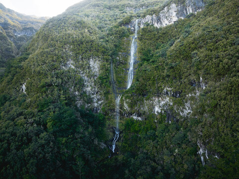 Aerial view of the PR17 Pinaculo e Folhadal waterfall cascading down a steep rocky cliff covered in dense green forest and lush vegetation in Serra de Agua, Madeira, Portugal.