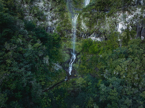 Aerial view of PR17 Pinaculo e Folhadal waterfall cascading down a steep rocky cliff surrounded by dense green forest and lush vegetation in Serra de Agua, Madeira, Portugal.