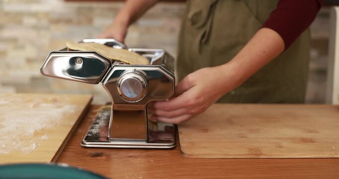 Young woman roll out the dough at home using pasta machine while preparing fresh tagliatelle - Handmade healthy food and italian culture concept