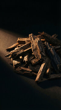A close-up captures a pile of fragrant oud wood chips, emanating an inviting earthy aroma. the dark aesthetic setting accentuates the texture and detail of the natural, luxury product.