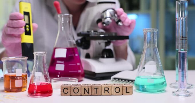 Word Control on wooden cubes among flasks of color reagent liquids in lab. Woman scientist works with microscope and digital meter in laboratory