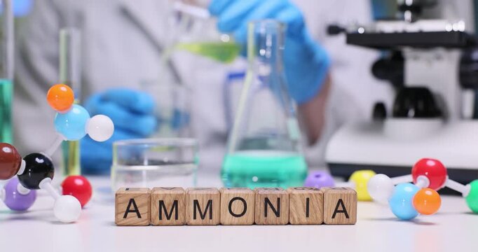 Word Ammonia spelled with wooden blocks against molecular structure models and flask on desk. Female researcher conducts tests in medical center