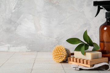 Obraz premium Spray bottle with plant branch, soap and cleaning brush on table near grunge wall