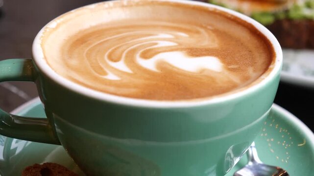 Close up motion of latte art coffee in a teal mug on saucer with spoon.