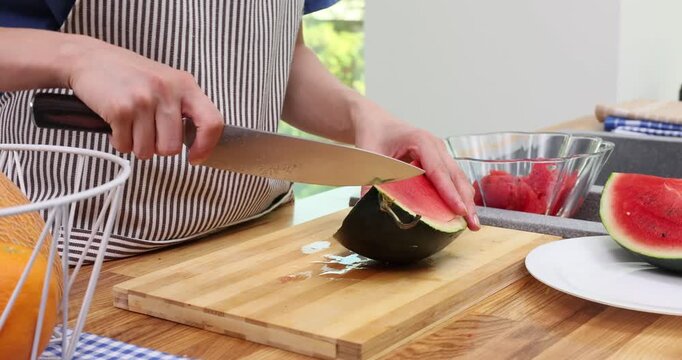 Chef slices watermelon on cutting board trimming rind with knife. Cook separates juicy cubes setting fruit pieces into bowl for serving time-lapse