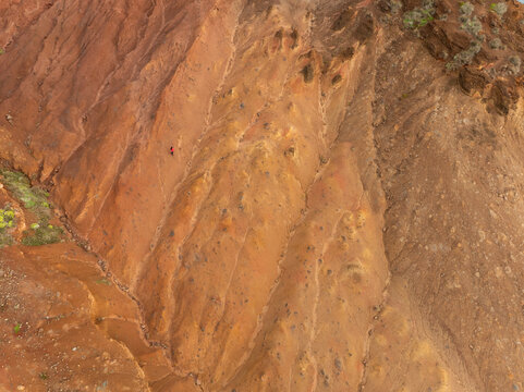 Aerial view of the reddish volcanic cliffs of Ponta de Sao Lourenco with a hiker in a red jacket on the steep slopes in Canical, Madeira, Portugal.