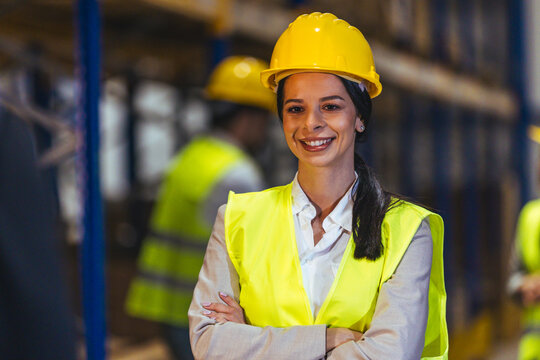 Female Site Manager Wearing Hard Hat And High-Visibility Safety Vest Smiling In Warehouse
