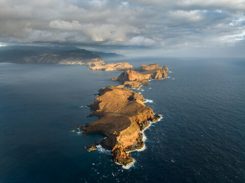 Aerial view of Ponta de Sao Lourenco peninsula with rugged volcanic cliffs and crashing waves under a dramatic cloudy sky in Canical, Madeira, Portugal.