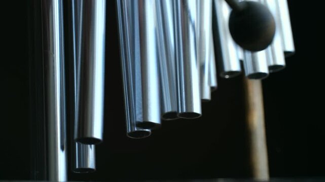 Close up musician playing bar chimes, percussion instrument also known as mark tree, with mallet producing shimmering sound effect against dark background. Playing a bar chimes percussion instrument