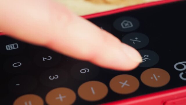 A close-up of a smartphone screen showing a calculator app with a finger entering numbers. The scene illustrates everyday computing, mobile productivity, and digital interaction with modern technology