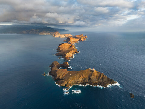 Aerial view of the Ponta de Sao Lourenco peninsula featuring rugged volcanic cliffs and crashing waves under a dramatic cloudy sky in Canical, Madeira, Portugal.