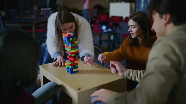 Young students are gathered around a table, intensely playing a block game. They are concentrating on pulling out blocks while building a tall, colorful tower.