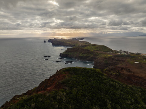 Aerial view of the rugged volcanic cliffs of Ponta de Sao Lourenco peninsula under a dramatic cloudy sky with sunbeams hitting the Atlantic Ocean in Canical, Madeira, Portugal.