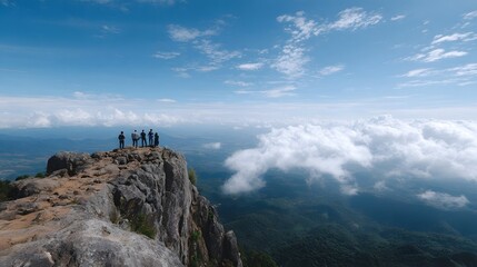 Fototapeta premium A small group of people stands on a towering rocky cliff overlooking a vast lush landscape partially submerged by a blanket of white clouds