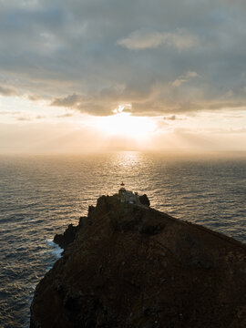 Aerial view of Ponta de Sao Lourenco lighthouse on a rugged cliff overlooking the Atlantic Ocean with golden sunbeams through clouds Canical, Madeira, Portugal.