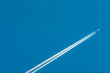 Airplane with white condensation tracks. Jet plane on clear blue sky with vapor trail. Travel by aeroplane concept. Trails of exhaust gas from airplane engine. Aircraft with white stripes. © Fahroni