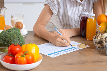 Young woman with healthy food making meal plan in kitchen, closeup. Diet concept © Pixel-Shot