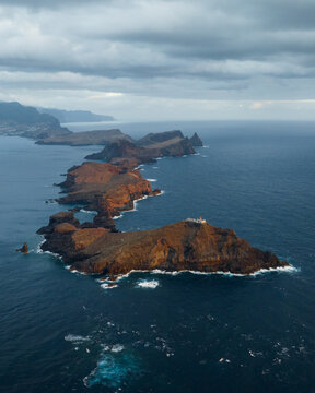Aerial view of the rugged volcanic cliffs of Ponta de Sao Lourenco and a small lighthouse surrounded by the Atlantic Ocean in Canical, Madeira, Portugal.