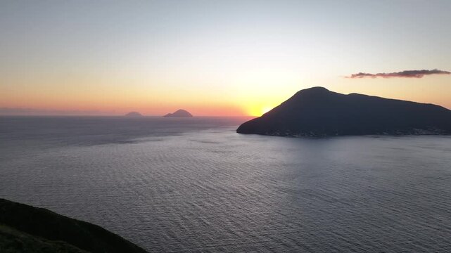 Aerial view from Lipari island approaching Salina island at sunset. Slow cinematic drone movement forward with gentle pan to the right over calm Mediterranean sea.