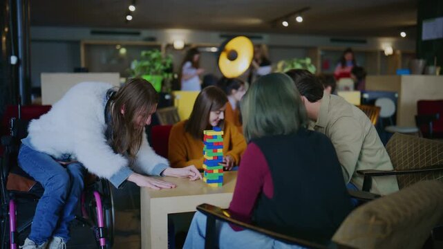 A diverse group of students plays a block stacking game in a casual setting. Young friends, including one in a wheelchair, enjoy a board game together.