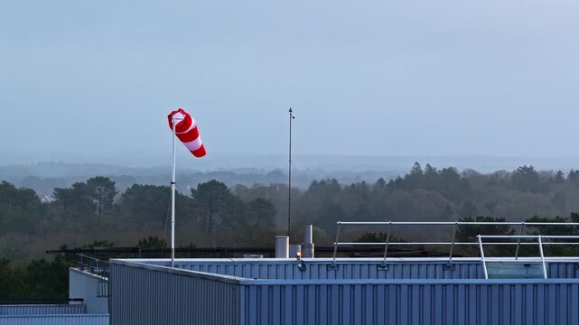 Windsock providing wind direction information from a factory roof, with trees in the distance