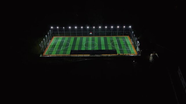 Aerial high-angle view of mini soccer field at night with bright stadium lights and green turf