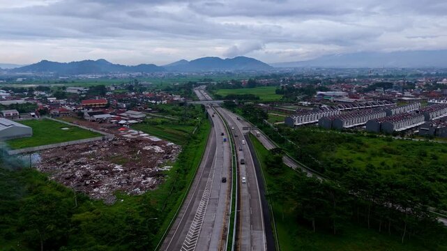 Wide panoramic shot of asphalt toll road cutting through suburban valley with hills in background