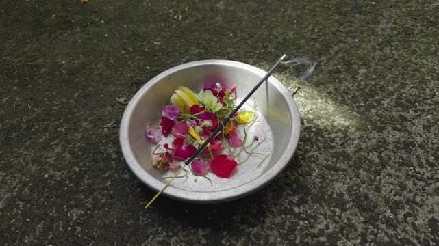 A close up of an aluminum plate filled with flowers and burning incense, releasing soft smoke. Used in Balinese Hindu prayer rituals, capturing sacred atmosphere and cultural spirituality.