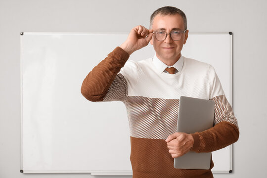 Male teacher with laptop near flipboard in classroom