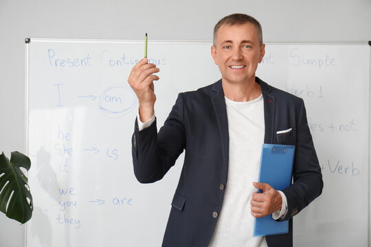 Male teacher with clipboard near flipboard in classroom