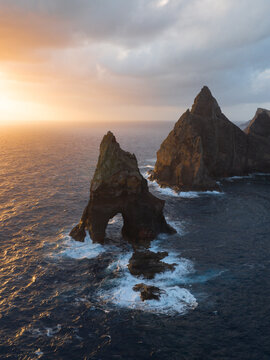 Aerial view of the Ponta de Sao Lourenco sea stacks and a natural rock arch during a golden sunset over the Atlantic Ocean in Canical, Madeira, Portugal.