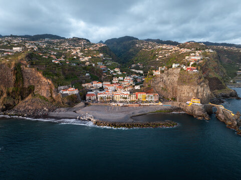 Aerial view of the coastal village of Ponta do Sol nestled between steep cliffs with white houses and a pebble beach by the Atlantic Ocean in Ponta do Sol, Madeira, Portugal.