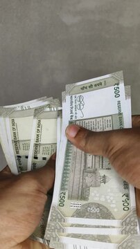 Hand counting bunch of indian currency, money or bank notes bundle of five hundred rupee. Financial, savings, economy, business, salary and investment concept background. Close up vertical top view.