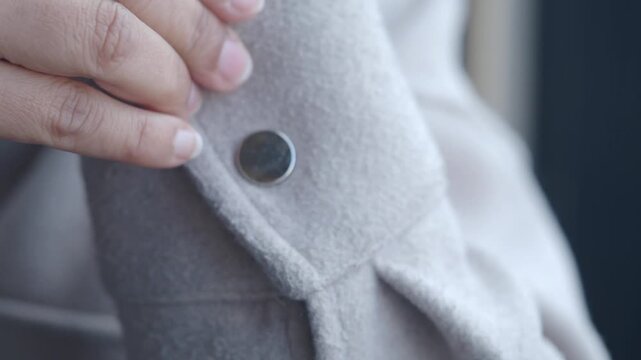 Person fastening metal snap button on grey wool coat sleeve close up view textile details.