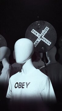 A group of faceless spinning mannequins and political statements contained on street signs on an endless loop.
