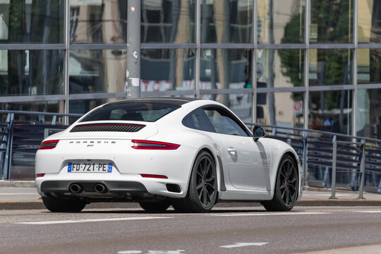 Nancy, France - May 29th 2020 : View on a white Porsche 991 Carrera S driving on a street with a glass facade in the background.