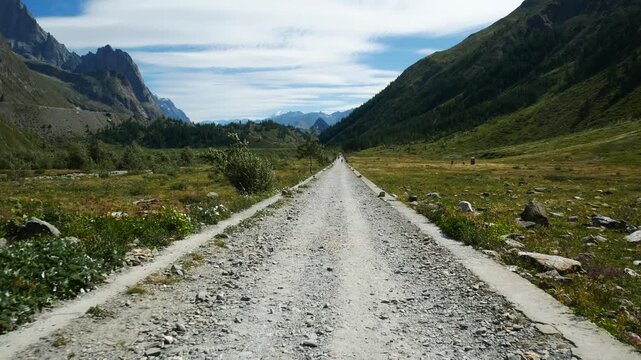 Walking on a hiking path in Veny Valley, Aosta Valley, Italy. Green vegetation and high mountains at both sides. Blue sky with white clouds on the background.