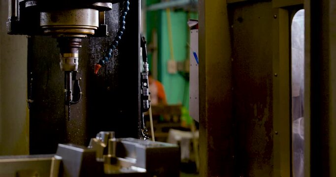 Asian male technician inspects CNC spindle area through machine opening, checking tool position, machining readiness, safety condition, maintenance detail, production workflow in industrial workshop.