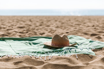 Obraz premium Summer beach accessories - straw hat, green towel on sea coast and sand background. Sunbathing, beach party, summer holiday picnic, travel, vacation minimal concept. Sun shadow and sunlight.