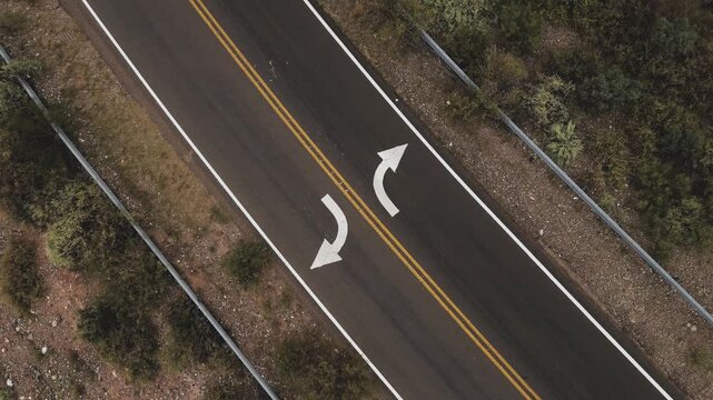 Spinning aerial view of white arrow signs on an asphalt road across the desert.