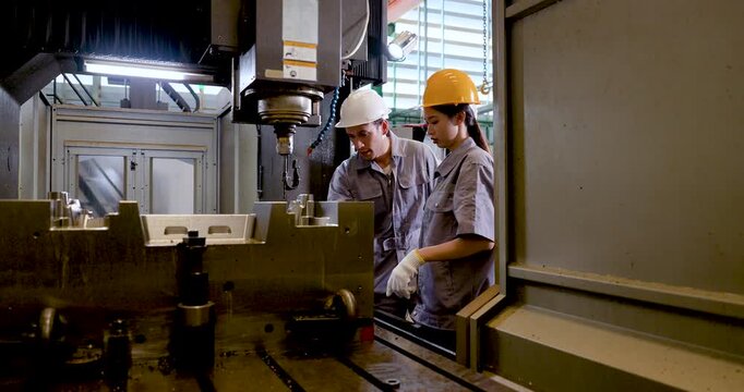 Asian factory engineer pair stands inside CNC machine area, reviewing fixture placement, tool path, safety clearance, machining status, production preparation, coordinated workflow in .