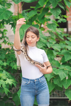 Young woman holding a python snake in an abandoned urban environment, wild concept