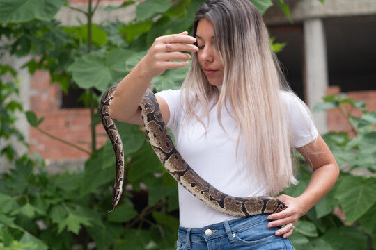 Young woman holding a python snake in an abandoned urban environment, wild concept